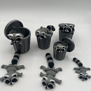 Peut inclure: Plusieurs figurines de ratons laveurs gris, certains à l'intérieur de petites poubelles avec des couvercles. Les ratons laveurs ont des marques noires et blanches et sont dans diverses poses. Les poubelles sont également grises.