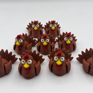 May include: A collection of nine brown turkey figurines with red combs, yellow beaks, and white eyes. The turkeys have detailed tail feathers and are arranged on a white surface.