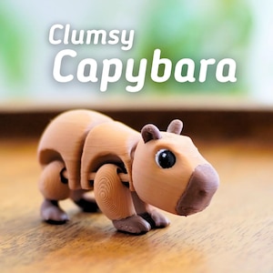 May include: A light brown, articulated capybara toy with the text "Clumsy Capybara". The toy has a detailed design with visible joints and a rounded body. The capybara is posed on a wooden surface, with a blurred green background.