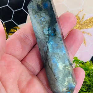 May include: A double-pointed, gray labradorite crystal with iridescent blue and green flashes. The crystal is about 5 inches long and is held in a hand.