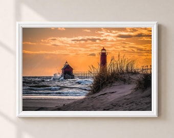 May include: A framed landscape photograph featuring a red lighthouse and a pier extending into a wavy sea under a golden sunset sky. The foreground shows a sandy dune covered with tall, dry beach grass, while the horizon glows with warm orange light.