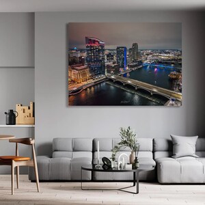 May include: An aerial view of a city skyline at night. The city is lit up with lights, and there is a river running through the middle of the city. There are several bridges crossing the river.