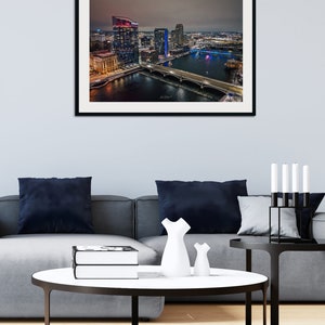 May include: An aerial view of a city skyline at night. The buildings are lit up in various colors, and the river below is reflecting the lights. There are several bridges crossing the river.