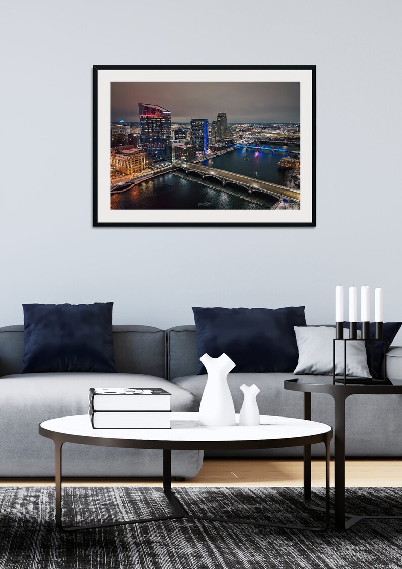 May include: An aerial view of a city skyline at night. The buildings are lit up in various colors, and the river below is reflecting the lights. There are several bridges crossing the river.