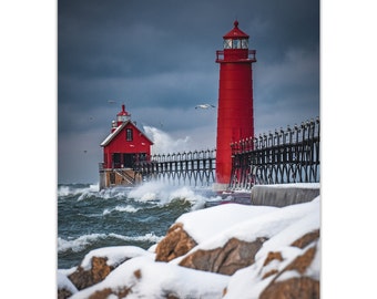 May include: A red lighthouse stands tall on a pier with crashing waves in the foreground. The lighthouse is surrounded by snow-covered rocks. The sky is a dramatic gray with dark clouds.