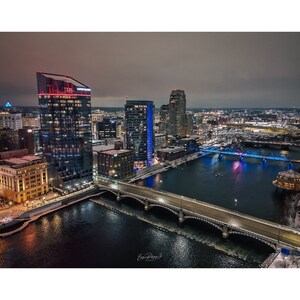 May include: An aerial view of a city skyline at night with a river flowing through it. The city is lit up with lights, and there are several bridges crossing the river. The river is frozen over in some places.