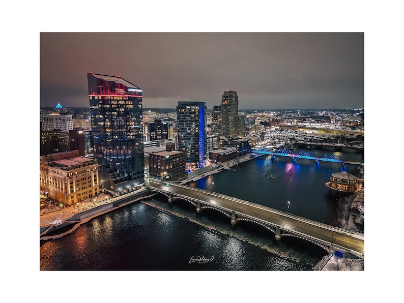 May include: An aerial view of a city skyline at night with a river flowing through it. The city is lit up with lights, and there are several bridges crossing the river. The river is frozen over in some places.