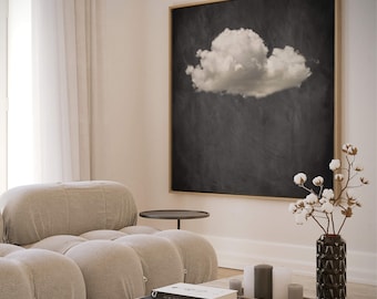 May include: A living room interior with a light beige sectional sofa, a black coffee table, and a framed black and white print of a cloud. A vase with cotton stems sits on a table with candles and books.