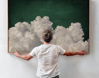 May include: A person hangs a framed painting on a white wall. The painting depicts a large, fluffy white cloud formation against a dark green background.