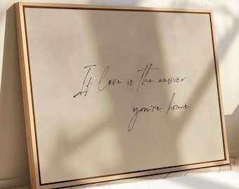 May include: A beige canvas print with a wooden frame. The print features the text "If love is the answer you're home" in black cursive script.