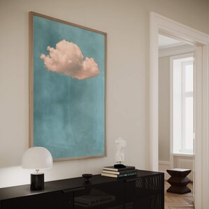 May include: A framed print of a single pink cloud against a blue sky. The print is hanging on a white wall above a black dresser with a white lamp and a white sculpture on top.