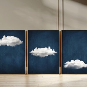 Op de afbeelding: Drie ingelijste prints met een donkerblauwe achtergrond en witte wolken. De wolken hebben verschillende vormen en maten.