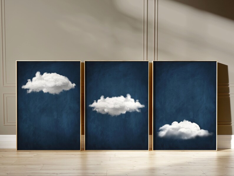 Op de afbeelding: Drie ingelijste prints met een donkerblauwe achtergrond en witte wolken. De wolken hebben verschillende vormen en maten.