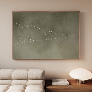 Könnte beinhalten: Ein rechteckiges Wandbild mit einem gedämpften olivgrünen Hintergrund und einer weichen, wolkigen Textur. Eine große Schar kleiner, weißer Vögel ist im Flug dargestellt und in einer V-Formation über die Mitte der Leinwand angeordnet.