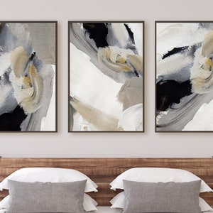 Op de afbeelding: Drie abstracte schilderijen in zwarte, witte en beige lijsten. De schilderijen tonen abstracte vormen en swirls in grijstinten, zwart en beige.