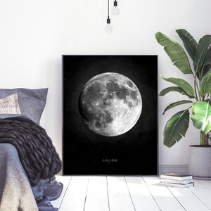 Op de afbeelding: Zwart-witte print van een volle maan met de tekst "LA LUNA" onderaan. De print is ingelijst en hangt aan een witte muur.
