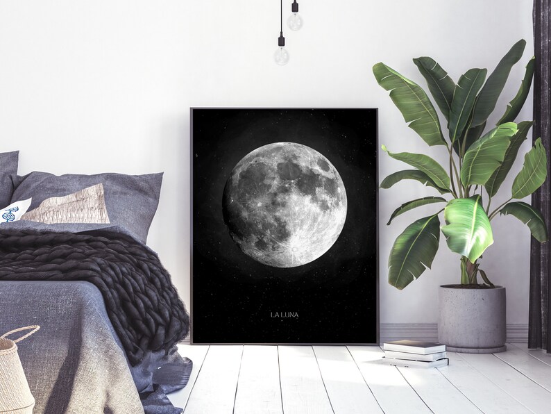 Op de afbeelding: Zwart-witte print van een volle maan met de tekst "LA LUNA" onderaan. De print is ingelijst en hangt aan een witte muur.