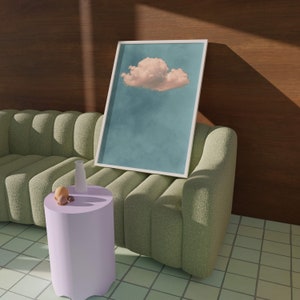 May include: A green tufted sofa with a white framed picture of a pink cloud in a blue sky. A small purple side table with a white bottle and fruit on top sits in front of the sofa.