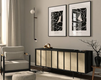 May include: A living room interior with a beige armchair, a black side table with a book on it, a black cabinet with beige panels, and two black and white abstract art prints on the wall.