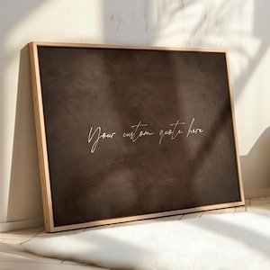 May include: A rectangular wall art piece featuring a dark brown, textured background enclosed in a light-colored wooden frame. The center of the artwork displays the white cursive text "Your custom quote here" written in a thin, elegant script.