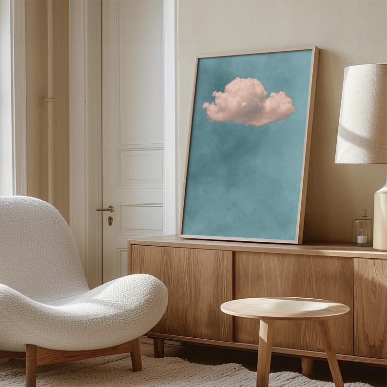 May include: A framed print of a single pink cloud against a blue sky. The print is hanging on a wall above a wooden cabinet.
