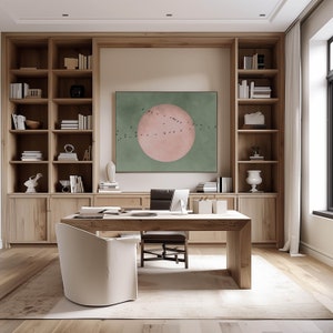 May include: A home office with a large wooden desk and a chair. The desk has a large painting of a pink circle with birds flying around it on a green background. The room has built-in wooden shelves with books and decor.