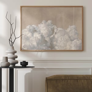 May include: A framed print of a large, fluffy cloud formation against a light beige background. The clouds are white and grey, and they fill the entire frame.