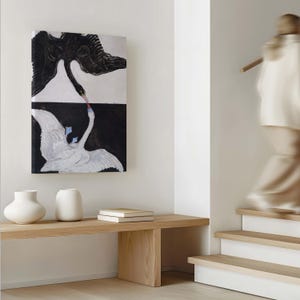 May include: A black and white painting of two swans with their necks intertwined. The painting is framed and hanging on a white wall above a wooden bench.