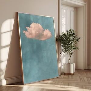 May include: A framed print of a single pink cloud against a blue sky. The print is in a gold frame and is hanging on a white wall.