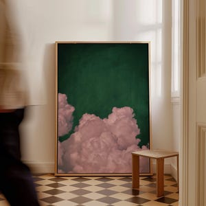 以下が含まれることがあります： 濃い緑色の背景にピンクの雲の形成が描かれた額装されたプリント