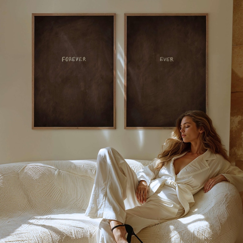 Puede incluir: Dos impresiones art&iacute;sticas enmarcadas con las palabras "FOREVER" y "EVER" en letras blancas. Las impresiones tienen un fondo marr&oacute;n oscuro y est&aacute;n en marcos de color marr&oacute;n claro. Una persona con un traje blanco est&aacute; sentada en un sof&aacute; blanco.