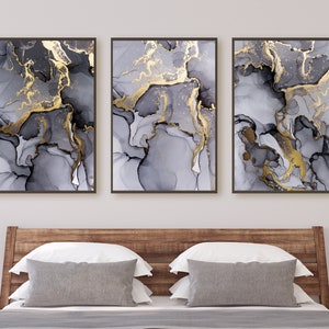 Op de afbeelding: Drie ingelijste abstracte kunstprints met een marmermotief in grijs en goud. De prints zijn in zwarte lijsten en zijn in een rij op een witte muur gerangschikt.