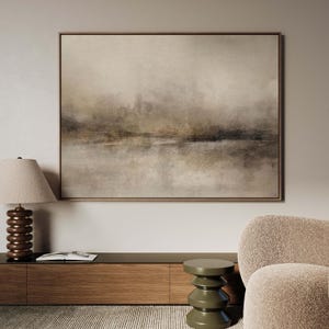 May include: Abstract landscape painting in neutral tones. The artwork features a blurred, atmospheric depiction of a body of water and a distant horizon. The painting is framed in a light brown wooden frame, adding a touch of warmth.