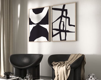 May include: Two black and white abstract art prints in wooden frames hanging on a white wall above two black chairs with a brown throw blanket on one of the chairs.