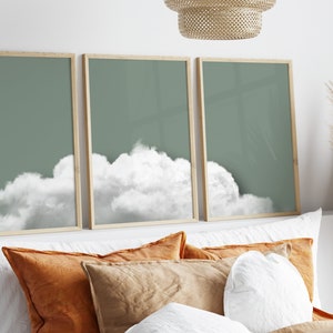 Peut inclure: Trois impressions encadrées avec un fond vert mat et un nuage blanc dans chacune. Les impressions sont disposées horizontalement sur un mur blanc au-dessus d'un lit avec des oreillers orange et bruns.