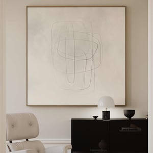 Op de afbeelding: Een minimalistisch abstract schilderij met zwarte lijnen op een witte achtergrond, hangend aan een muur boven een zwarte kast met een witte lamp en een zwarte kom.