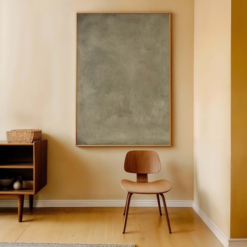 May include: A room with a large framed abstract painting in shades of gray and brown. A wooden chair with a curved back and a low wooden cabinet with a woven basket on top are in the foreground. The walls are painted in a warm, neutral tone.