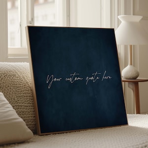 May include: A framed navy blue canvas with the text "Your custom quote here" in a cursive font. The artwork is displayed indoors, leaning against a cream-colored surface, with a window and lamp in the background.