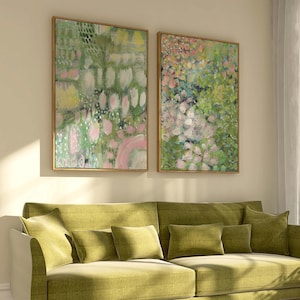 Puede incluir: Dos pinturas abstractas enmarcadas con un tema floral. La obra de arte presenta una mezcla de pinceladas verdes, rosas y blancas, sobre un fondo claro. Los marcos son de un tono cálido de madera natural. Las pinturas se exhiben sobre un sofá verde.