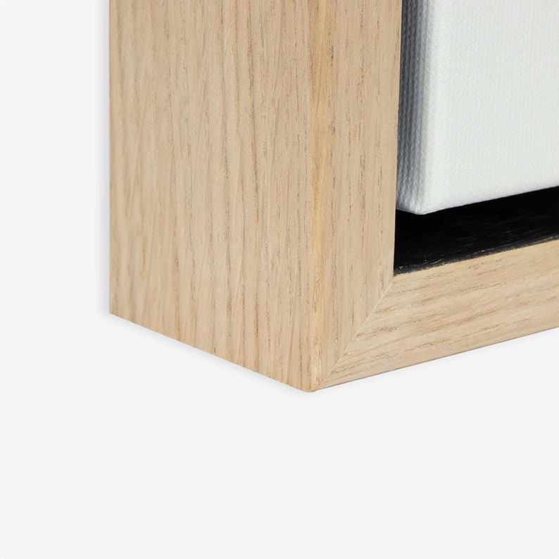 K&ouml;nnte beinhalten: Nahaufnahme der Ecke eines Bilderrahmens aus hellem Holz. Der Rahmen besteht aus Naturholz mit sichtbarer Maserung. Der Rahmen umgibt eine wei&szlig;e Leinwand.