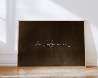 May include: A framed art print with a dark brown background and the handwritten text "how lucky are we" in white script. A small white heart is to the right of the text. The frame is a light wood color.