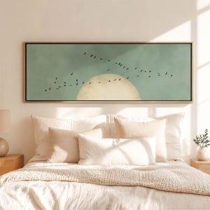 Könnte beinhalten: Ein rechteckiges Wandkunstwerk mit minimalistischem Design. Das Kunstwerk zeigt einen Schwarm schwarzer Vögel, die vor einem hellblauen Himmel fliegen, mit einer großen, hellgelben Sonne. Der Rahmen ist hellbraun.