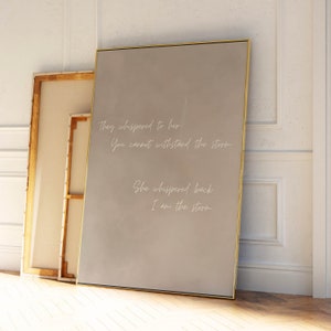 May include: A beige canvas print with gold framing features a quote in white script: "They whispered to her You cannot withstand the storm She whispered back I am the storm."