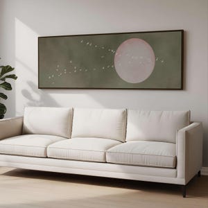 Puede incluir: Una impresión enmarcada de arte mural que presenta un gran círculo rosa y una bandada de pájaros blancos sobre un fondo verde apagado. La obra de arte está sobre un sofá blanco de tres cojines.