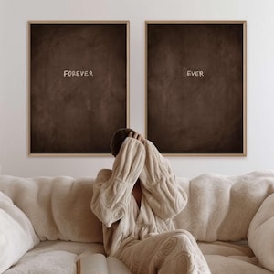 Puede incluir: Dos obras de arte enmarcadas con las palabras "FOREVER" y "EVER" en escritura blanca sobre un fondo marr&oacute;n oscuro. Los marcos son de color marr&oacute;n claro. Una persona est&aacute; sentada en un sof&aacute; beige.