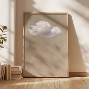 Puede incluir: Una impresión enmarcada de una sola nube blanca sobre un fondo beige. La impresión está en un marco de madera simple.