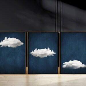 Op de afbeelding: Drie ingelijste prints met een donkerblauwe achtergrond en witte wolken. De wolken hebben verschillende vormen en maten.