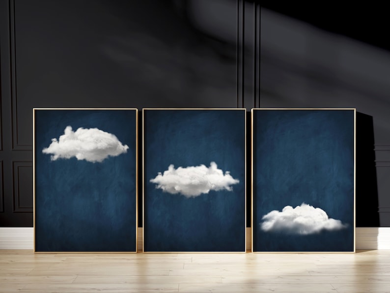Op de afbeelding: Drie ingelijste prints met een donkerblauwe achtergrond en witte wolken. De wolken hebben verschillende vormen en maten.