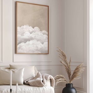 May include: A framed print of a beige and white abstract painting featuring a stylised depiction of clouds. The painting is hanging on a white wall in a living room setting.