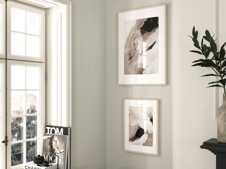 May include: Two framed abstract art prints in a neutral color palette of beige, brown, and black. The prints are hung on a white wall.